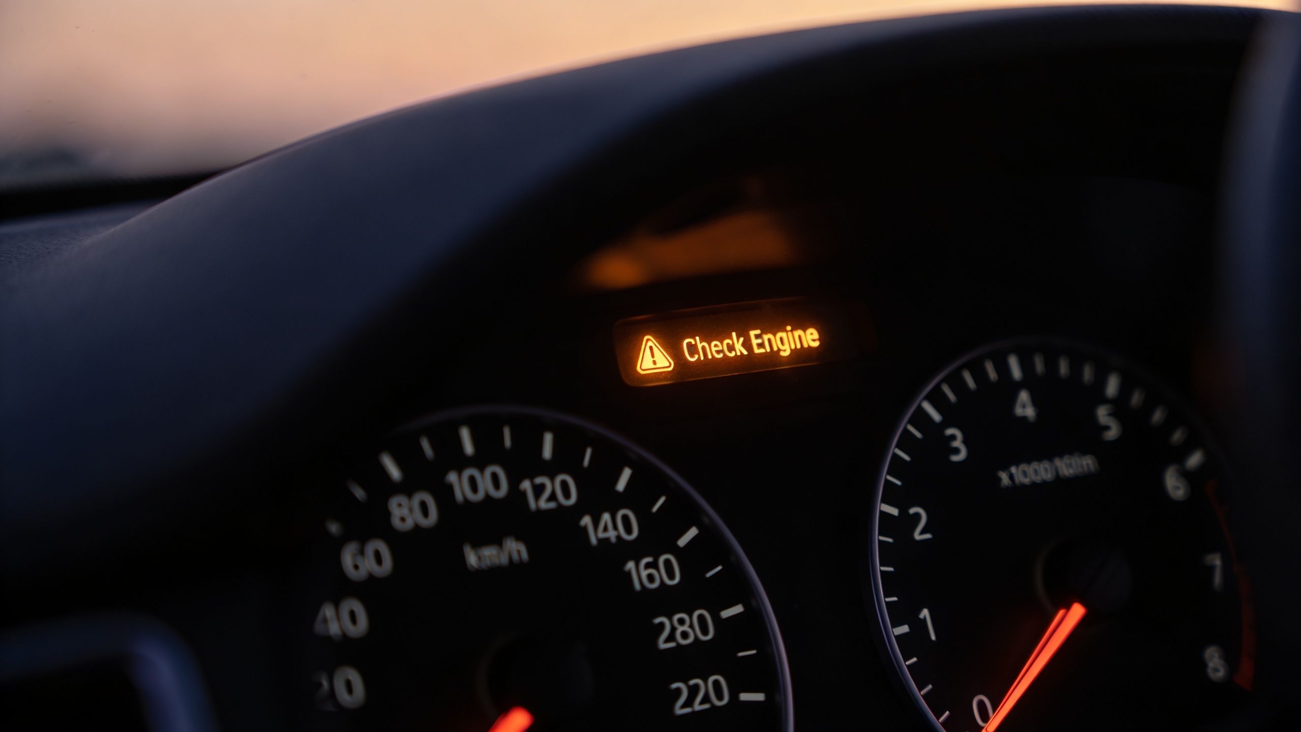 A close-up view of a car dashboard showing an illuminated yellow warning light that says Check Engine.