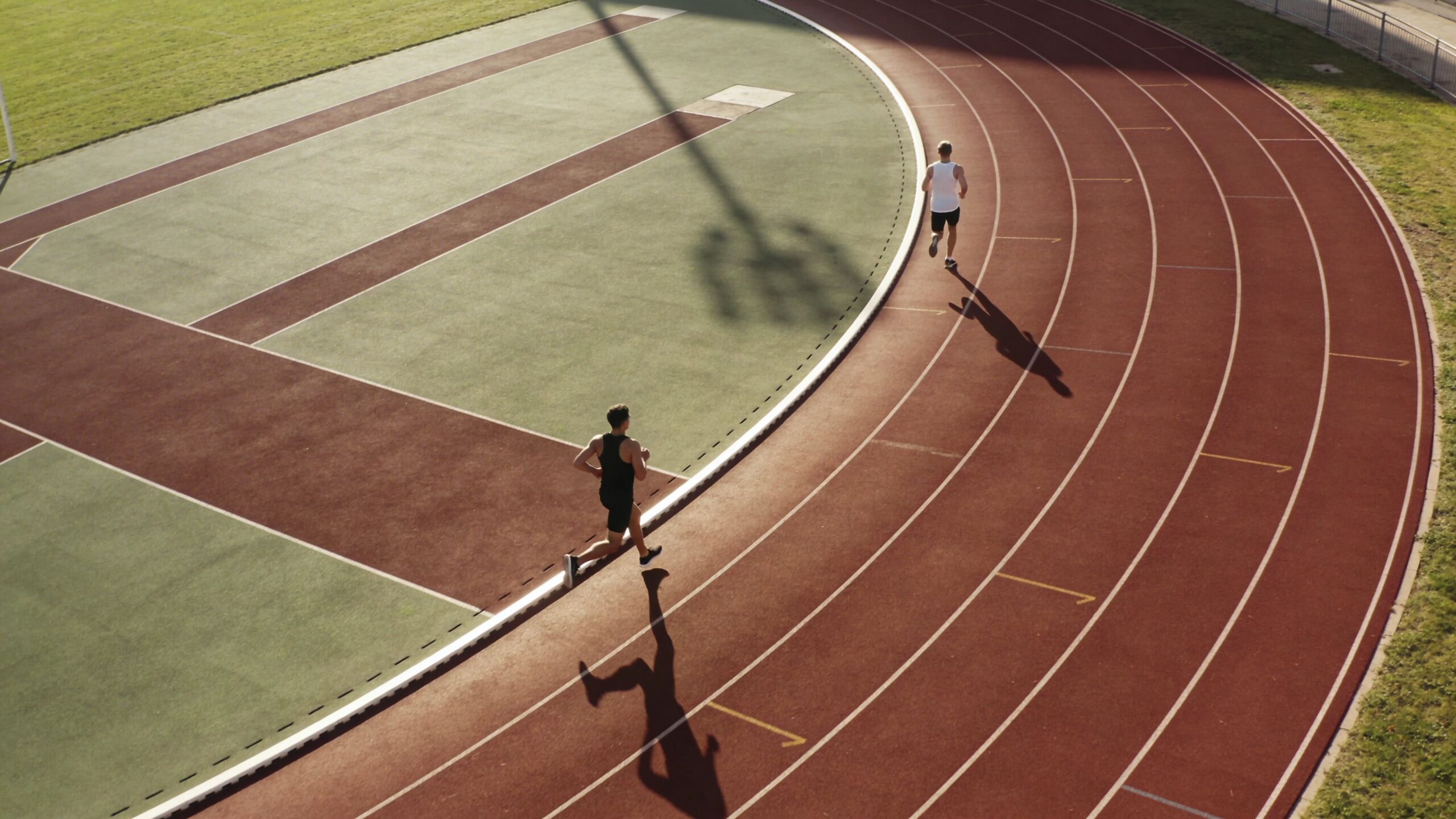 Two athletes jogging on a professional running track at a stadium during a sunny day
