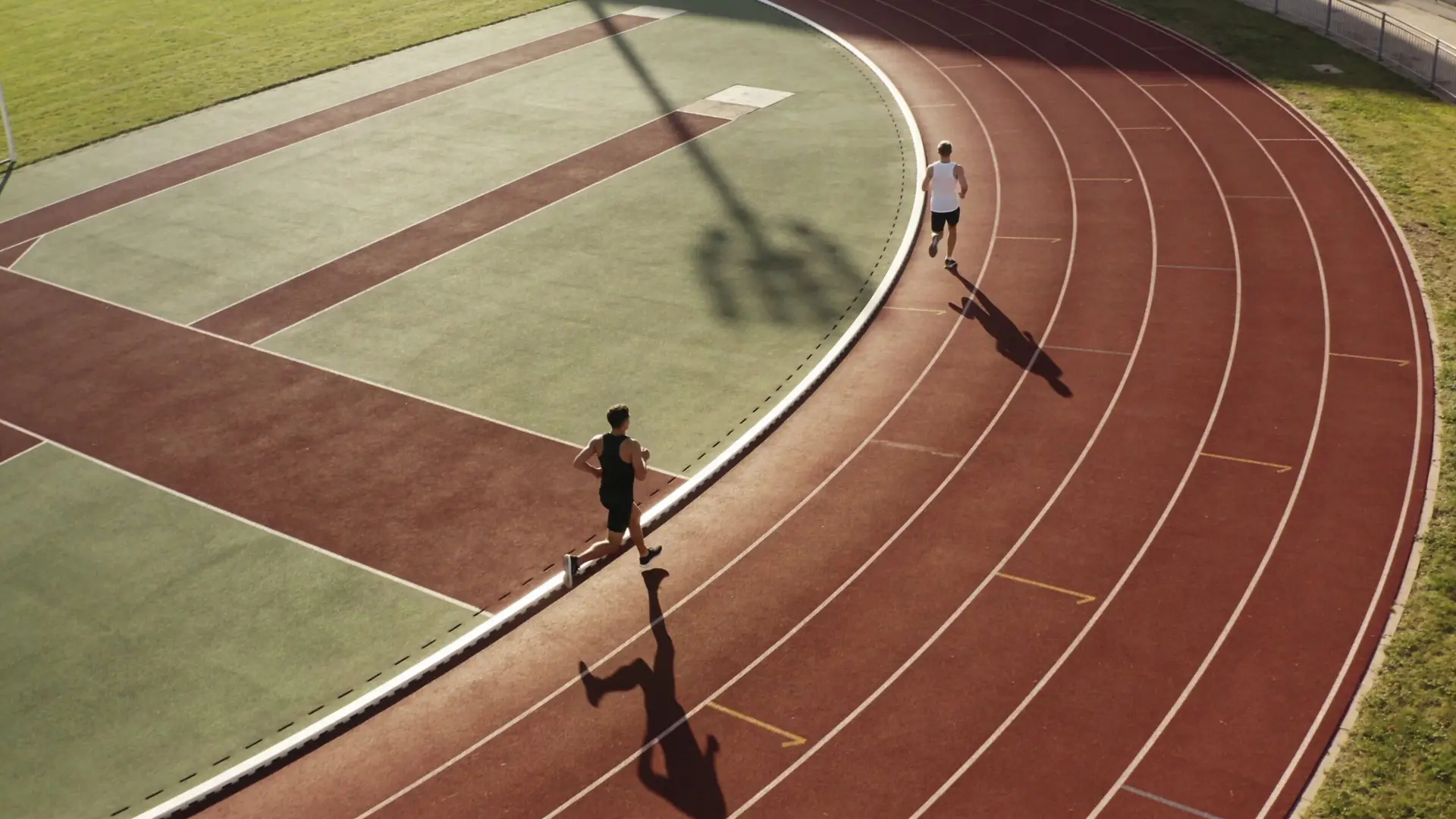 Two athletes jogging on a professional running track at a stadium during a sunny day