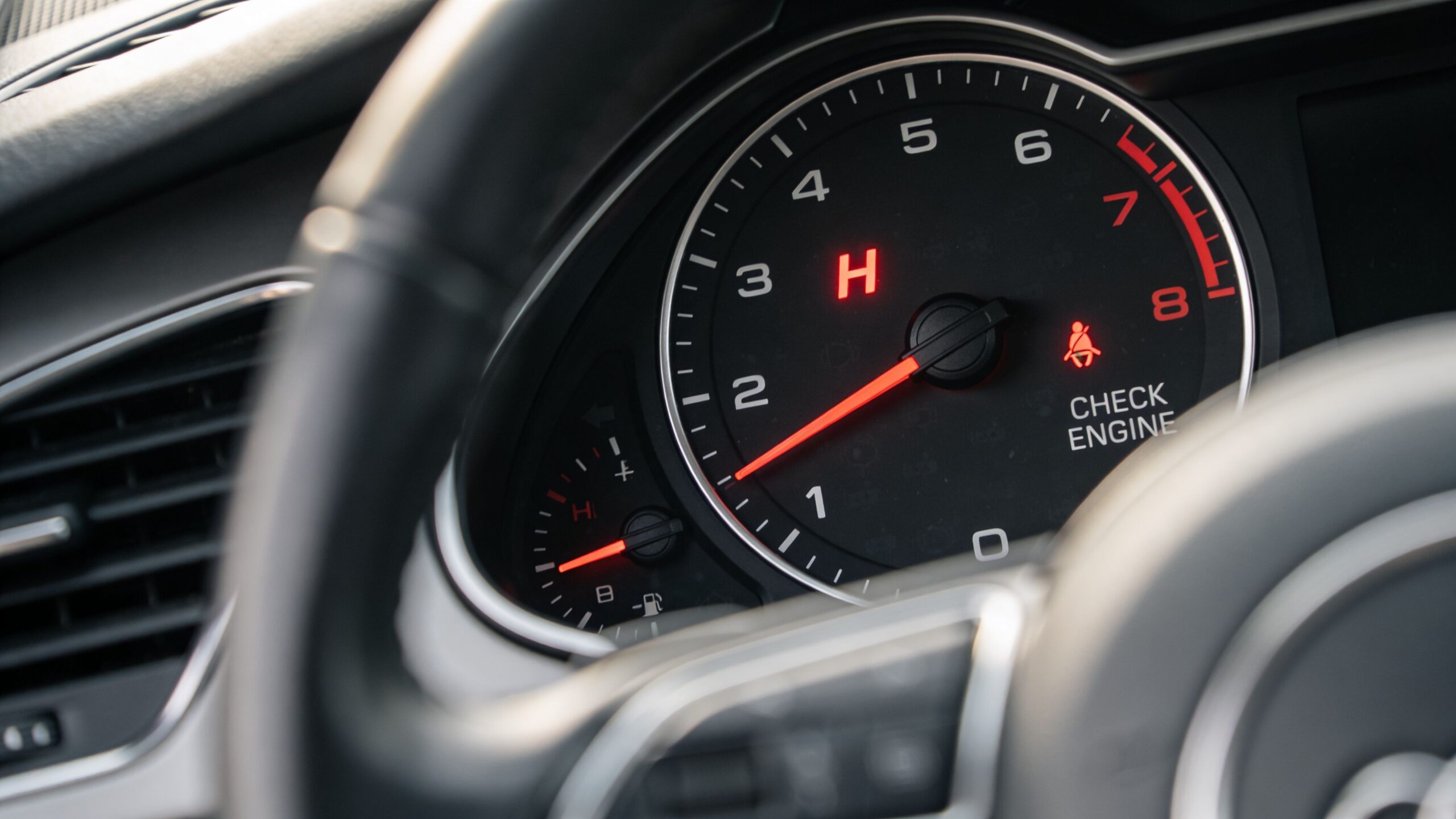A close-up view of a car dashboard showing the tachometer gauge with an illuminated engine warning light.