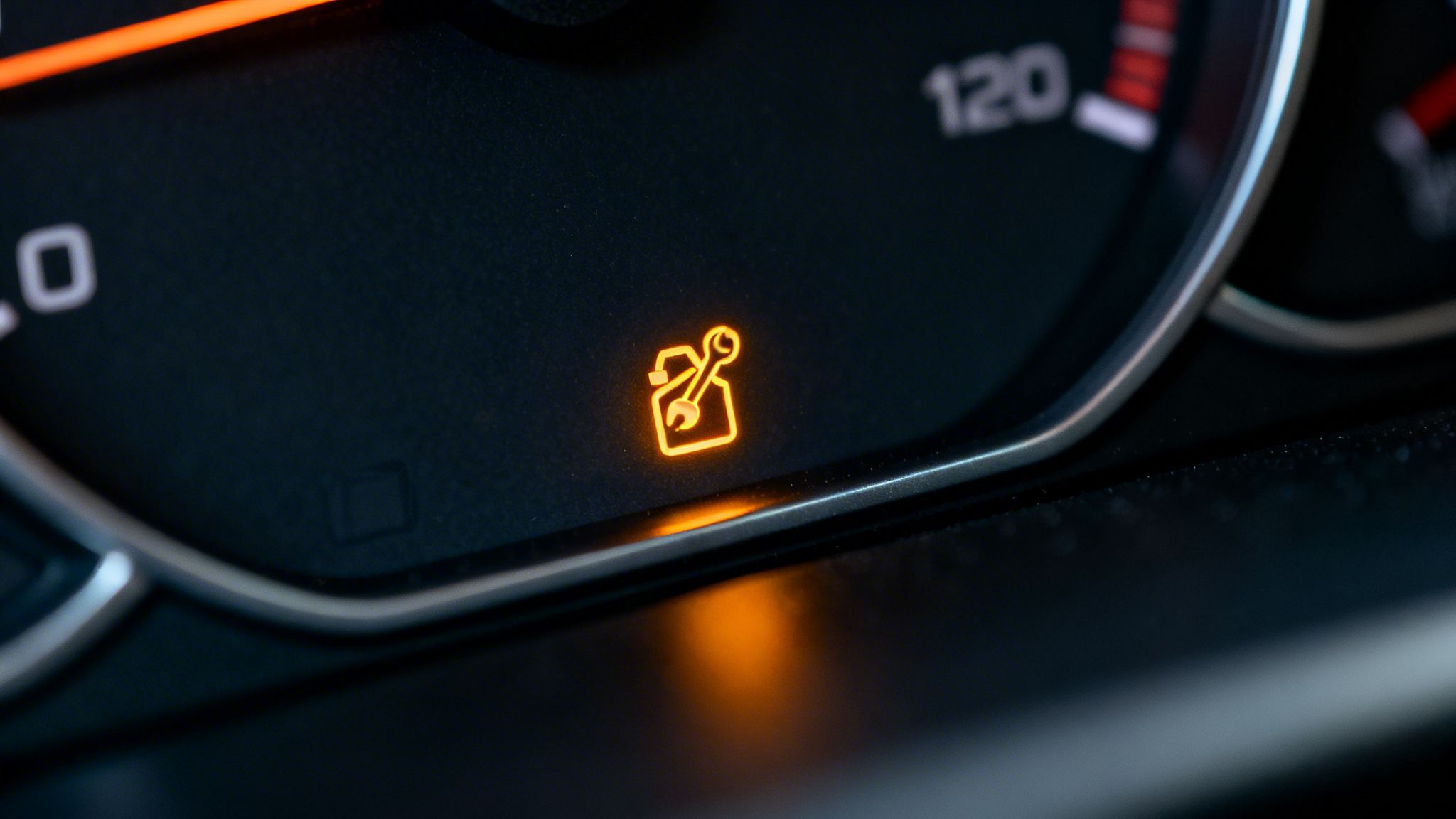 A close-up view of an illuminated dashboard warning light showing a wrench symbol inside a fuel canister.
