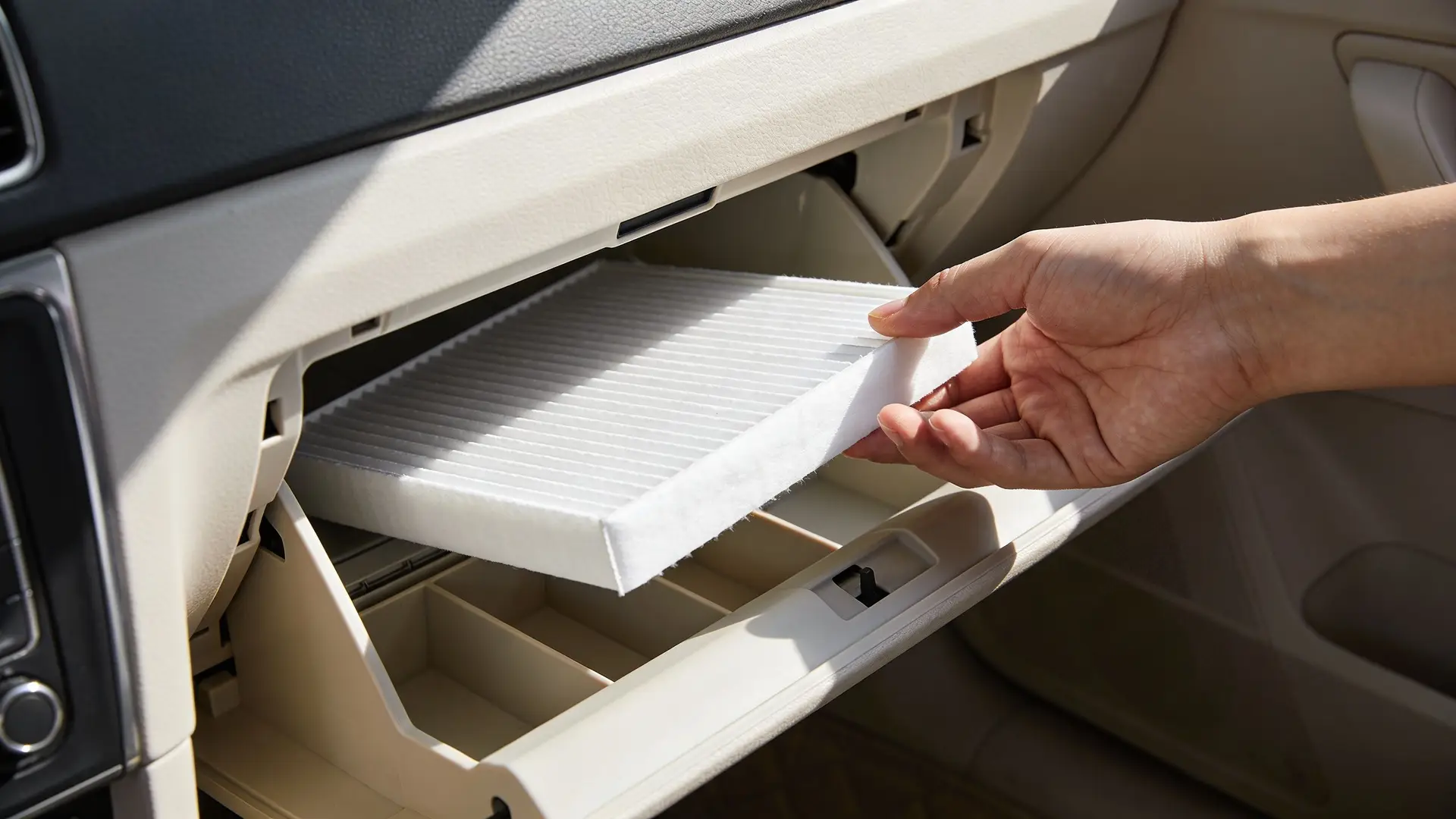 A person replacing the cabin air filter inside the glove compartment of a modern car interior.