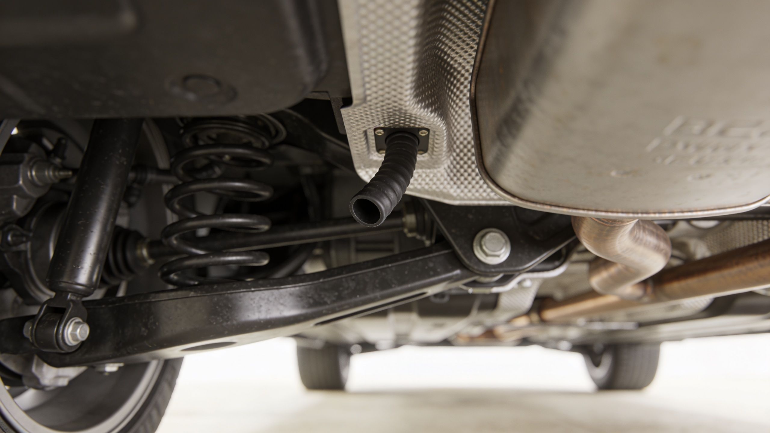 A close-up view of a car undercarriage showing the rear suspension and an open rubber drain hose.