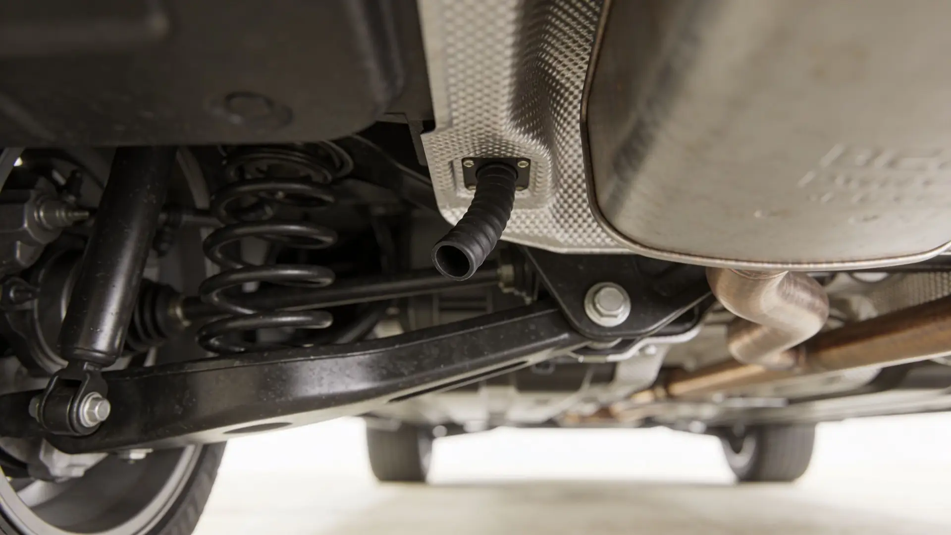A close-up view of a car undercarriage showing the rear suspension and an open rubber drain hose.