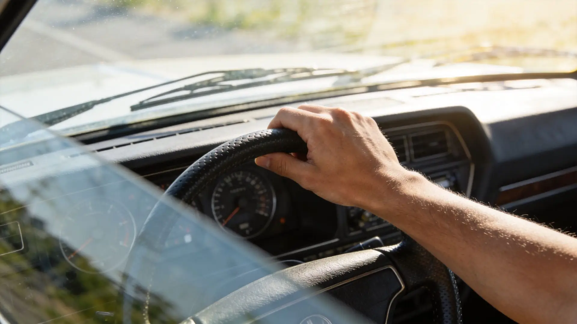 A close-up view of a driver's hand resting on the leather-wrapped steering wheel inside a car