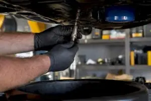 Gloved mechanic draining oil under car