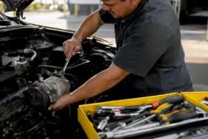 Technician removing AC compressor in workshop