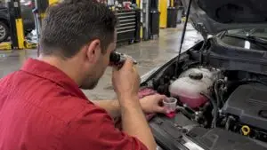 Technician testing coolant beside an open hood